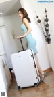 A woman in a blue dress standing next to a white suitcase.