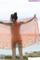 A woman standing on a beach holding up a colorful scarf.