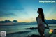 A woman standing on a rock by the ocean at sunset.