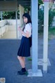 A woman in a school uniform leaning against a pole.